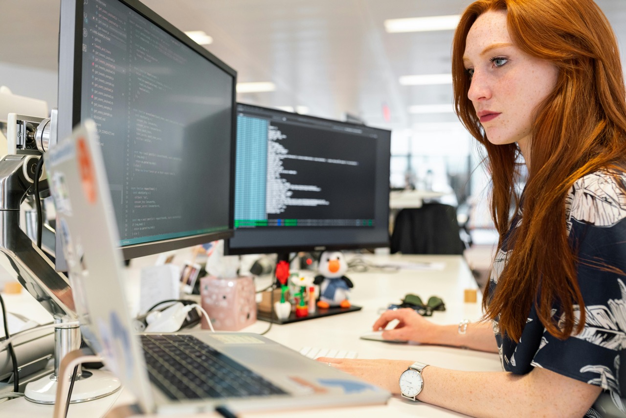 A woman sitting at her desk with two monitors.